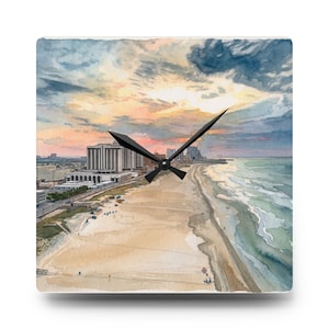 Könnte beinhalten: Eine quadratische Wanduhr mit einem Aquarellgemälde einer Küstenstadt-Skyline bei Sonnenuntergang. Die Szene zeigt einen Sandstrand am Ozean mit hohen Gebäuden entlang der Küste unter einem bewölkten Himmel. Schwarze Uhrzeiger sind mittig.