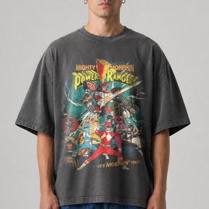 May include: Dark grey t-shirt with a graphic of the Mighty Morphin Power Rangers. The design includes the Power Rangers team, a Megazord, and the text "Mighty Morphin Power Rangers" and "It's Morphin' Time!"