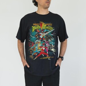 K&ouml;nnte beinhalten: Schwarzes T-Shirt mit einer farbenfrohen Grafik der Mighty Morphin Power Rangers. Das Design zeigt das Power Rangers-Team, einen Roboter und den Text "Mighty Morphin Power Rangers" und "It's Morphin' Time!"