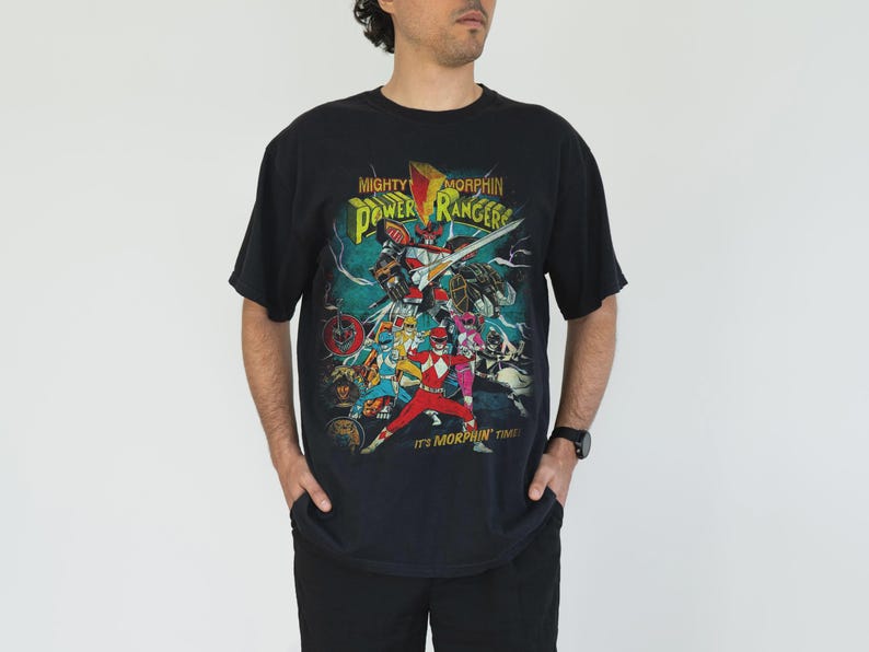 K&ouml;nnte beinhalten: Schwarzes T-Shirt mit einer farbenfrohen Grafik der Mighty Morphin Power Rangers. Das Design zeigt das Power Rangers-Team, einen Roboter und den Text "Mighty Morphin Power Rangers" und "It's Morphin' Time!"