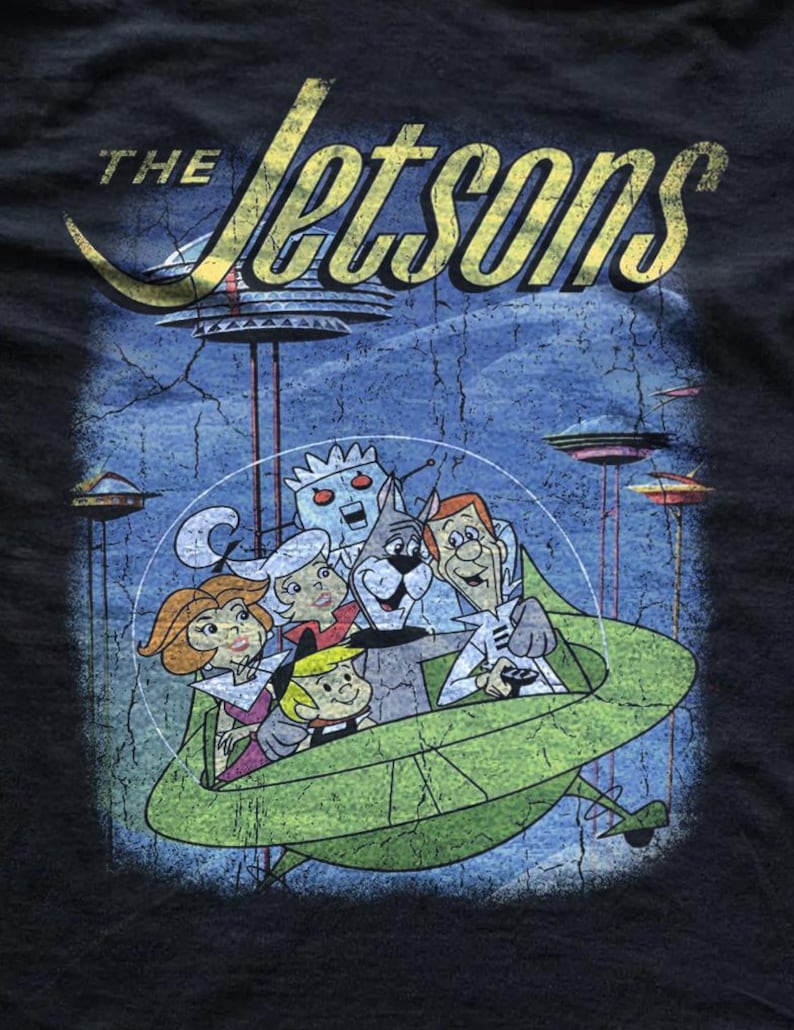 May include: Black t-shirt featuring a distressed graphic of the Jetsons family in a green spaceship. The text "The Jetsons" is in yellow, with a retro space-age design. The background shows flying saucers and a blue sky.