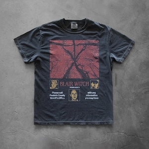 May include: Dark grey t-shirt with a red and black tree graphic. The shirt features the text "BLAIR WITCH PROJECT" and a call to the Frederick County Sheriff's Office for information.