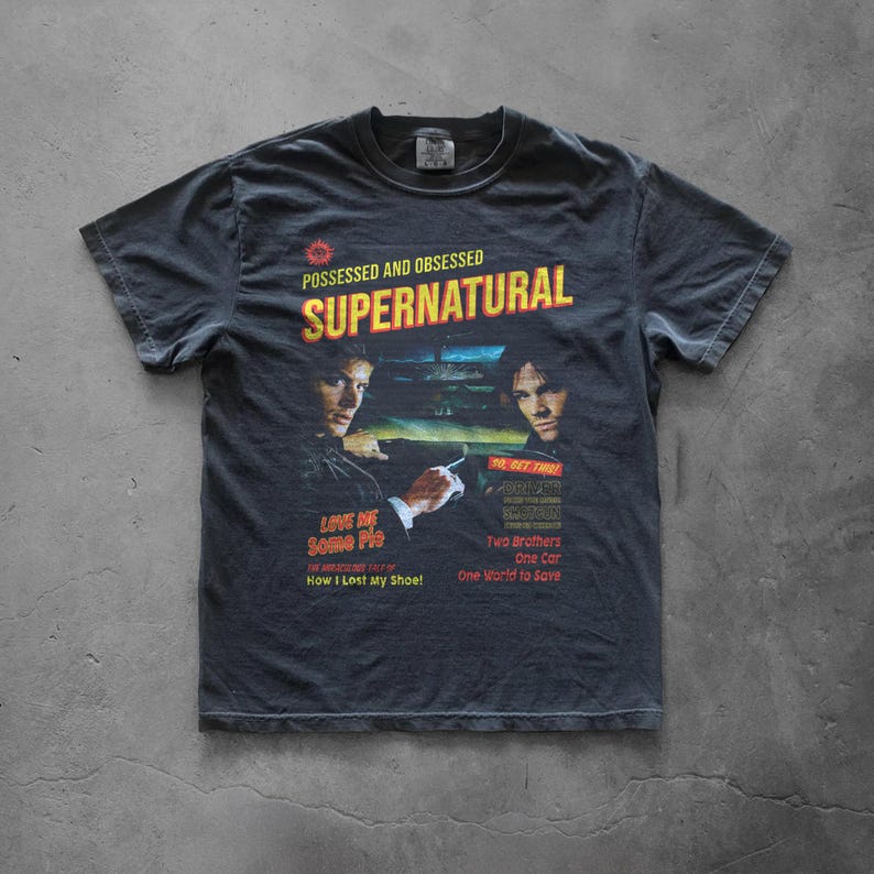 May include: A charcoal gray short-sleeve t-shirt featuring a graphic print with the text SUPERNATURAL, POSSESSED AND OBSESSED, LOVE ME SOME PIE, HOW I LOST MY SHOE, SO GET THIS, DRIVER PICKS THE MUSIC, SHOTGUN SHUTS HIS CAKEHOLE, TWO BROTHERS, ONE CAR, ONE WORLD TO SAVE.