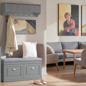 May include: A gray entryway storage bench with two drawers and a cushioned seat, paired with a matching wall-mounted shelf featuring three fabric storage bins and five metal hooks. A beige coat hangs from one hook, and a white pillow sits on the bench.