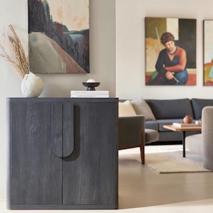 May include: A dark charcoal gray wooden cabinet with two doors featuring integrated vertical handles. The cabinet has a smooth, rounded top edge and a visible wood grain texture. It stands as a standalone storage unit with a clean, rectangular design.