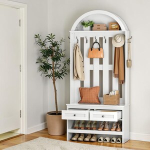 May include: A white entryway storage unit with an arched top, hooks, and shoe storage. It features a coat, purse, hat, and scarf hanging on the hooks. There are two drawers and shelves filled with shoes. A potted plant and a rug are in the foreground.