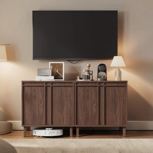 May include: A dark brown wooden cabinet with four doors, a black TV mounted above it, and decorative items on top. A white robot vacuum cleaner is visible beneath the cabinet. A lamp and a framed picture are also present.