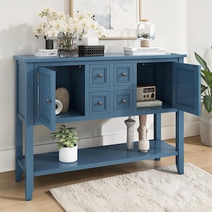 May include: A blue wooden console table featuring two side cabinets with open doors, four central drawers with small round knobs, and a lower storage shelf. The piece is finished in a solid blue paint and stands on four straight legs.