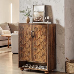 May include: A wooden shoe cabinet with a distressed finish and decorative carved pattern. The cabinet has two doors with metal handles and a lower shelf holding several pairs of sandals. The cabinet is set on rounded feet.
