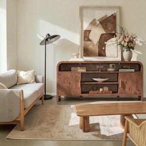 May include: A light gray sofa with a wooden frame, a black floor lamp, a wooden coffee table, and a long wooden media console with burl wood grain. The console features open shelving, two cabinets, and decorative items including a vase of flowers.