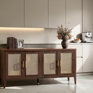 May include: A rectangular wooden sideboard featuring four cabinet doors with light-colored woven cane panels and vertical gold-toned metal handles. The sideboard stands on four tapered legs and is topped with a row of books and a dark vase.