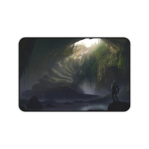 May include: Rectangular mouse mat featuring a digital art landscape of a cave with a figure standing on a rock. The scene includes a waterfall, lush green vegetation, and a light source from above.