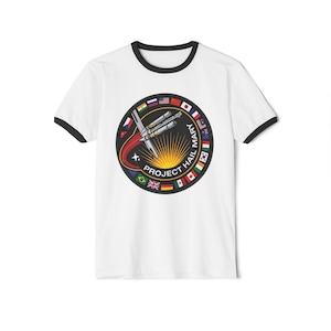 May include: White t-shirt with black trim. The circular graphic features a rocket, sunburst, and flags, with the text "PROJECT HAIL MARY". A red trail extends from the rocket, representing its trajectory.