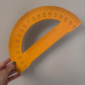 Peut inclure: Un rapporteur orange vif, gradué de 0 à 180 degrés. Cet instrument de géométrie présente un bord droit et un bord incurvé. Il est utilisé pour mesurer les angles, avec des mesures en degrés, une unité de mesure angulaire standard.