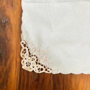 Op de afbeelding: Een witte linnen tafelrunner met een delicate kantzoom en een geborduurd bloemenmotief.