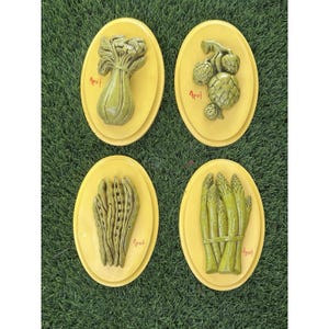 May include: Four oval wall plaques with yellow backgrounds and raised green vegetable sculptures. Each plaque features a different vegetable: celery, artichokes, peas in a pod, and asparagus. The red text Apsit is printed on each yellow surface.