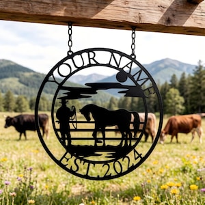 Puede incluir: Letrero de metal negro con la silueta de un vaquero y un caballo dentro de un marco circular. Las palabras "YOUR NAME" y "EST 2024" están recortadas. El letrero cuelga de cadenas sobre un fondo de campo y montañas.