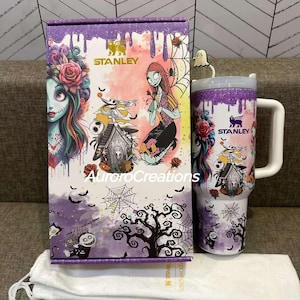 May include: A Stanley insulated tumbler and matching box featuring characters from The Nightmare Before Christmas. The tumbler has a white handle and lid, with a purple glitter rim. The box and tumbler have illustrations of Sally, Jack Skellington, and Zero.