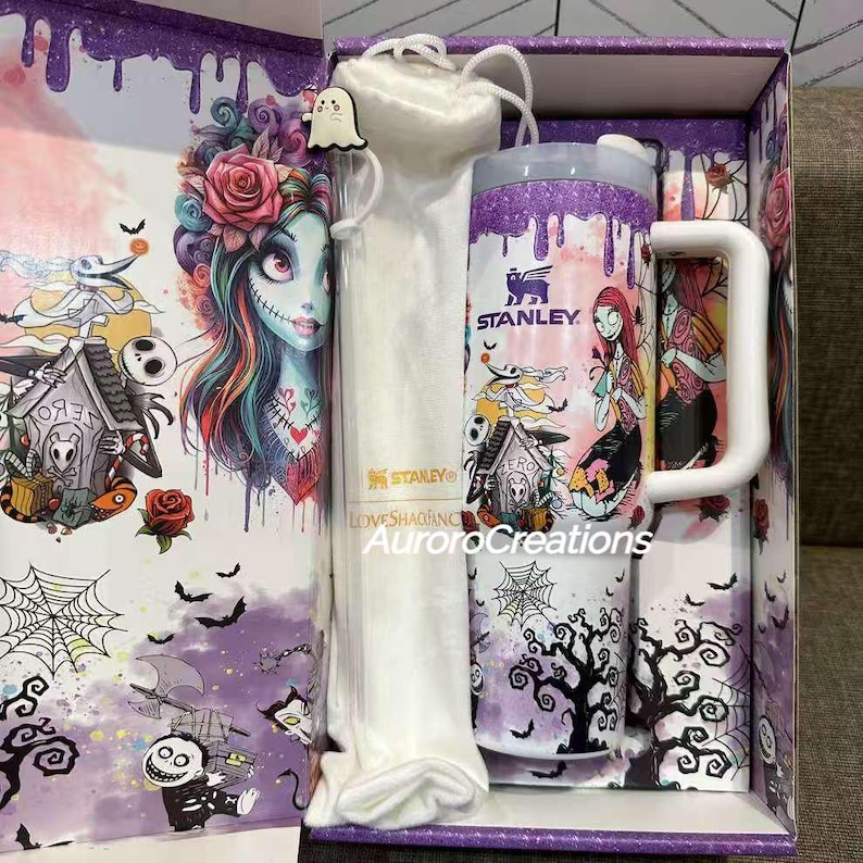 May include: A gift set featuring a Stanley mug and tumbler with a matching straw and carrying bag. The set has a purple and white color scheme with a spooky cartoon design. The box has a matching design with the text "AuroraCreations".