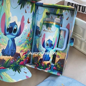 Pu&ograve; includere: Una tazza Stanley blu e rosa con il personaggio Stitch di Lilo & Stitch, all'interno di una confezione regalo abbinata. La tazza ha un manico blu e un coperchio trasparente con cannuccia. La scatola e la tazza sono decorate con una scena di foresta e farfalle.