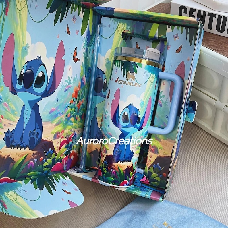 Pu&ograve; includere: Una tazza Stanley blu e rosa con il personaggio Stitch di Lilo & Stitch, all'interno di una confezione regalo abbinata. La tazza ha un manico blu e un coperchio trasparente con cannuccia. La scatola e la tazza sono decorate con una scena di foresta e farfalle.