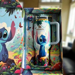 Pu&ograve; includere: Un bicchiere da viaggio Stanley con un personaggio dei cartoni animati blu, presentato in una scatola abbinata. Il bicchiere ha un manico bianco e un coperchio argentato. La scatola e il bicchiere sono decorati con un'illustrazione colorata del personaggio in un ambiente forestale stravagante con farfalle.