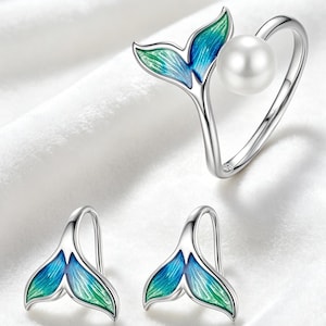 Op de afbeelding: Een sieradenset bestaande uit een ring en twee oorbellen. De ring heeft een witte parel en een zilveren walvisstaartmotief met blauw en groen emaille. De twee oorbellen zijn gevormd als zilveren walvisstaarten met blauw en groen emaille.