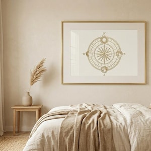May include: A bedroom scene with a neutral color palette. A large framed print of a compass hangs above a bed with beige bedding. A small wooden side table holds a vase with dried plants. A window with sheer curtains is on the left.