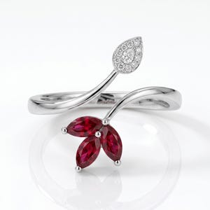 May include: A silver bypass ring featuring a floral-inspired design. One end displays three marquise-cut deep red rubies arranged like petals, while the other end features a teardrop-shaped setting encrusted with small round white diamonds.