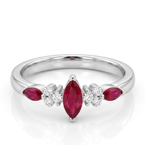 Peut inclure: Une bague en argent ornée d'un rubis central en forme de marquise, flanqué de deux rubis plus petits et de grappes de petits diamants ronds. Le design de la bague est symétrique et élégant.