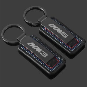 May include: Two black keychains with a rectangular leather base and a metal plate. The metal plate has the text "M3" or "M5" in silver. The leather base has blue, red, and white stitching.