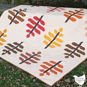 May include: A handmade quilt featuring a repeating leaf pattern in shades of red, yellow, orange, and brown on a cream background. The leaves are arranged diagonally across the quilt, with a dark brown stem. The quilt is bordered with a brown fabric.