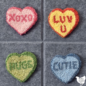Könnte beinhalten: Vier herzförmige Filz-Handarbeiten mit verschiedenen Farben und Botschaften. Das obere linke Herz ist rosa mit dem Wort "XOXO" in Weiß. Das obere rechte Herz ist gelb mit den Worten "LUV U" in Rot. Das untere linke Herz ist grün mit dem Wort "HUGS" in Weiß. Das untere rechte Herz ist blau mit dem Wort "CUTE" in Weiß.