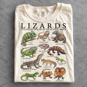 Könnte beinhalten: Ein cremefarbenes T-Shirt mit einem Grafikdruck mit der Aufschrift LIZARDS ILLUSTRATED SPECIES OF THE NATURAL WORLD. Das Design zeigt detaillierte Illustrationen verschiedener Echsen, darunter ein Chamäleon, eine Bartagame und ein Komodowaran.