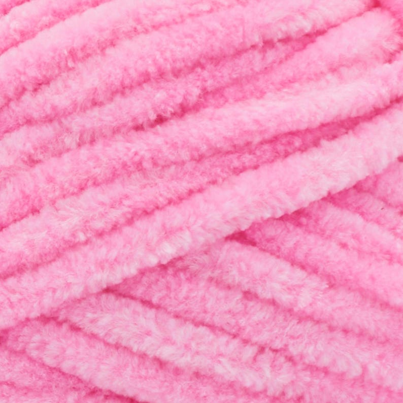May include: Close-up of a skein of soft, pink yarn. The yarn has a thick, plush texture with visible strands and a slightly fuzzy appearance. The colour is a vibrant, light pink, ideal for knitting or crocheting projects.