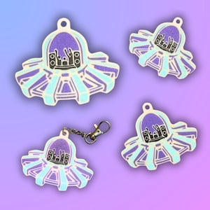May include: Four glittery, light blue and purple charms with a concert theme. Each charm features a stage design with speakers and a crowd. One charm is attached to a silver keychain with a lobster clasp.