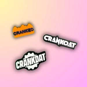 May include: Three colorful shoe charms with the words "CRANKED", "CRANKOAT", and "CRANKDAT" in bold, stylized fonts. The charms are in orange, black, and white, set against a gradient pink and yellow background.