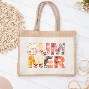 May include: A rectangular tote bag made of natural tan jute with two matching handles. The front features the word SUMMER in large block letters, each filled with a different colorful pattern including gingham, floral, and tropical motifs.