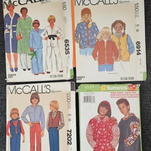 May include: Four vintage sewing pattern envelopes for children's clothing. The patterns are from McCall's and Butterick, featuring illustrations of various outfits. The envelopes are labeled "Kid's Casual" and include sizes. The image is on a gray surface.
