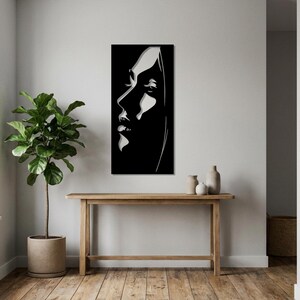 Op de afbeelding: Een rechthoekig zwart wandkunstobject met een contrastrijk wit silhouet van een gezicht in profiel. Het ontwerp gebruikt gedurfde negatieve ruimte om de gelaatstrekken, waaronder het oog, de neus en de lippen, te definiëren tegen een zwarte achtergrond.