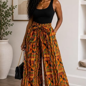 May include: A black sleeveless tank top paired with high-waisted wide-leg trousers featuring a vibrant geometric pattern in shades of orange, yellow, green, and black. The trousers include a matching fabric tie belt at the waist and side pockets.