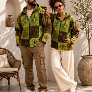 May include: Two hooded zip-up jackets featuring a patchwork design in shades of lime green and dark brown. The fabric is decorated with black floral and sun-like patterns. Each jacket includes a front zipper, a hood, and long sleeves with cuffs.