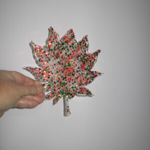 May include: A clear plastic leaf-shaped ornament with red and green glitter embedded inside.
