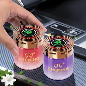 Könnte beinhalten: Zwei Auto-Lufterfrischer, einer rot und einer lila, mit goldfarbenen Deckeln und Böden. Jeder hat ein grünes Logo und den Text "CHEMING CAR PERFUME" in Gold. Der rote Erfrischer hat einen Farbverlauf, und der lila hat einen ähnlichen Verlauf.