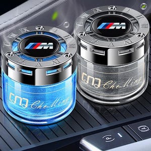 Könnte beinhalten: Zwei Auto-Lufterfrischer mit silbernen Oberteilen und blauen und grauen Basen. Die Oberteile zeigen das BMW-Logo und römische Ziffern. Der blaue Lufterfrischer trägt den Text "Che Ming".