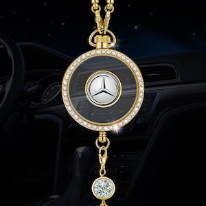 Può includere: Ciondolo per auto dorato con un pendente circolare con il logo Mercedes-Benz argentato. Il pendente è circondato da un anello di cristalli trasparenti e appeso a una catena dorata. Un cristallo scintillante pende sotto.