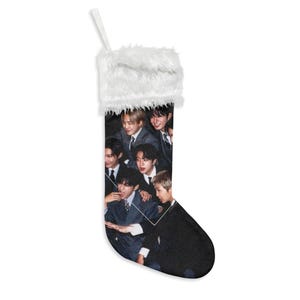 Peut inclure: Une chaussette de Noël avec un revers en fausse fourrure blanche et une boucle de suspension. Le corps de la chaussette présente un collage photographique imprimé de sept personnes vêtues de costumes sombres, disposées en portrait de groupe.