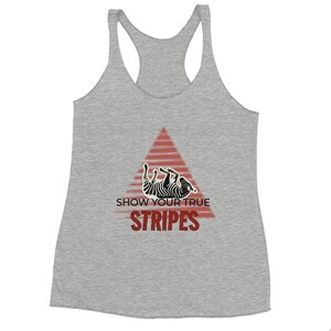 Peut inclure: Un débardeur gris avec un motif triangulaire rouge. Le motif présente une illustration de zèbre et le texte "SHOW YOUR TRUE STRIPES" en gras, en rouge. Le débardeur est fait d'une matière douce.