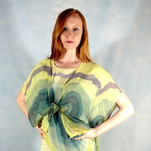 Puede incluir: Una mujer lleva un vestido de seda estampado en amarillo, verde y gris con un escote anudado. El vestido tiene una silueta fluida y un ajuste holgado.