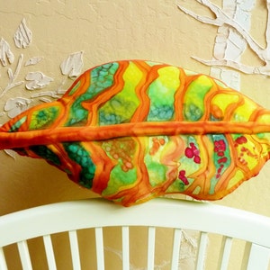 May include: A colorful leaf-shaped pillow with orange, yellow, green, and red accents. The pillow is made of fabric and has a quilted design.
